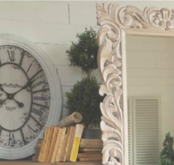 Decorative mirror with intricate carvings next to a clock and books on a shelf.