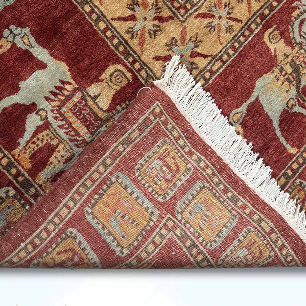 Close-up of a patterned red rug with white fringe on a plain background