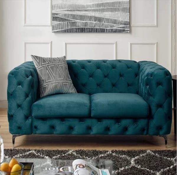 Teal velvet sofa with a patterned pillow in a living room setting.