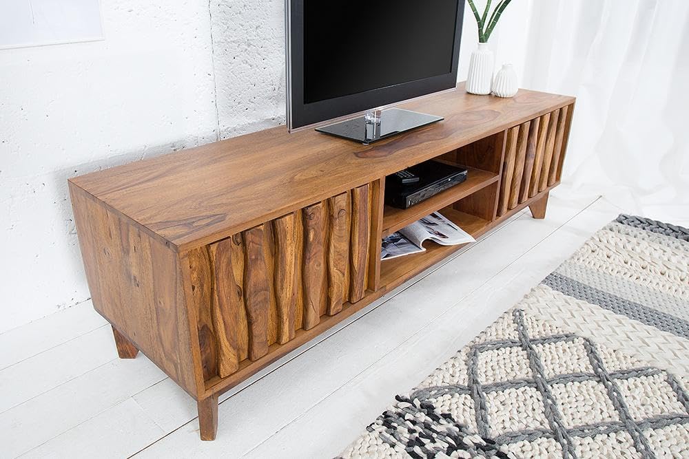 Wooden TV stand with a television on top in a room with a rug and white walls.
