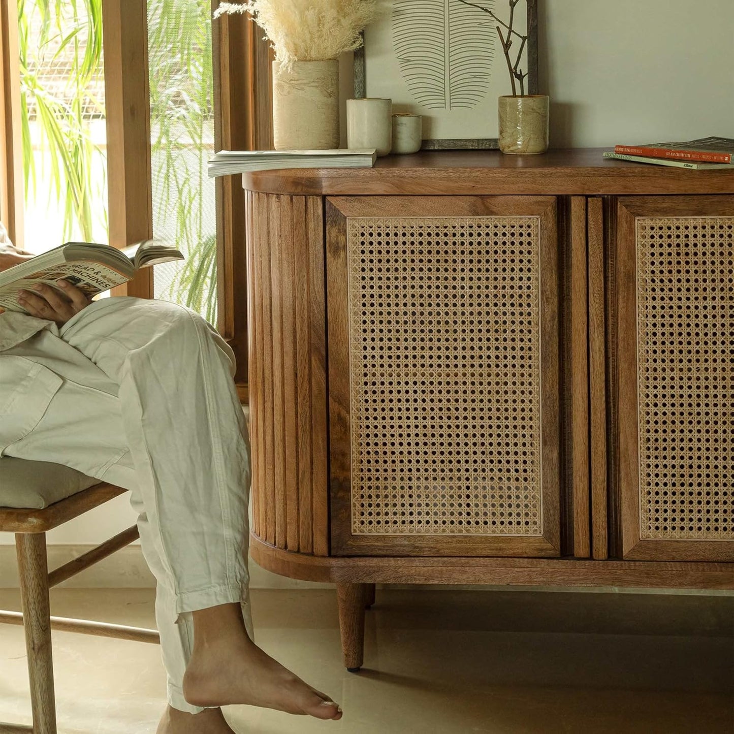 Person sitting on a chair with feet up on a wooden sideboard in a bright room.
