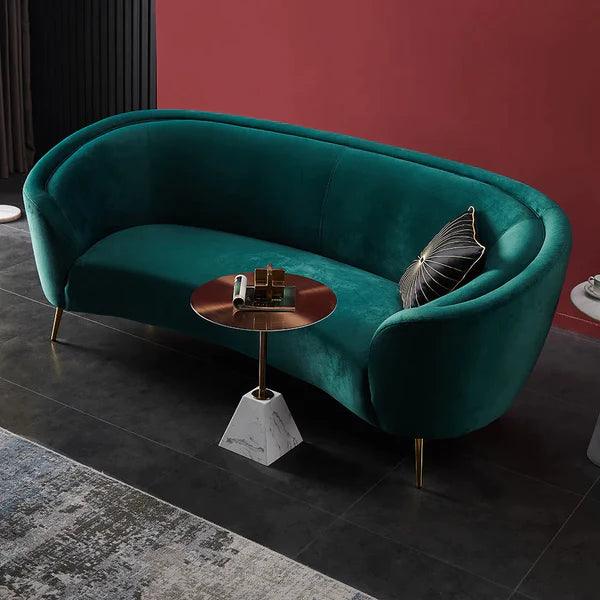 Teal velvet sofa with a small round table against a red wall.