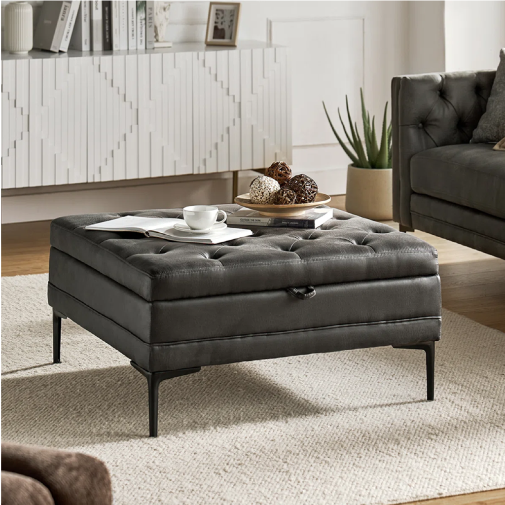 Gray tufted ottoman in a living room setting with a coffee table and decor items.