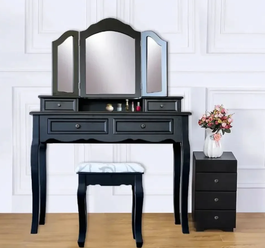 Black vanity table with mirror, stool, and nightstand against a white paneled wall.
