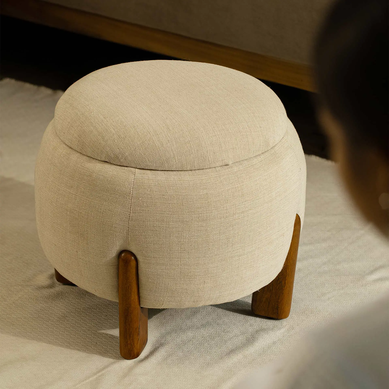 Beige ottoman with wooden legs on a light-colored floor