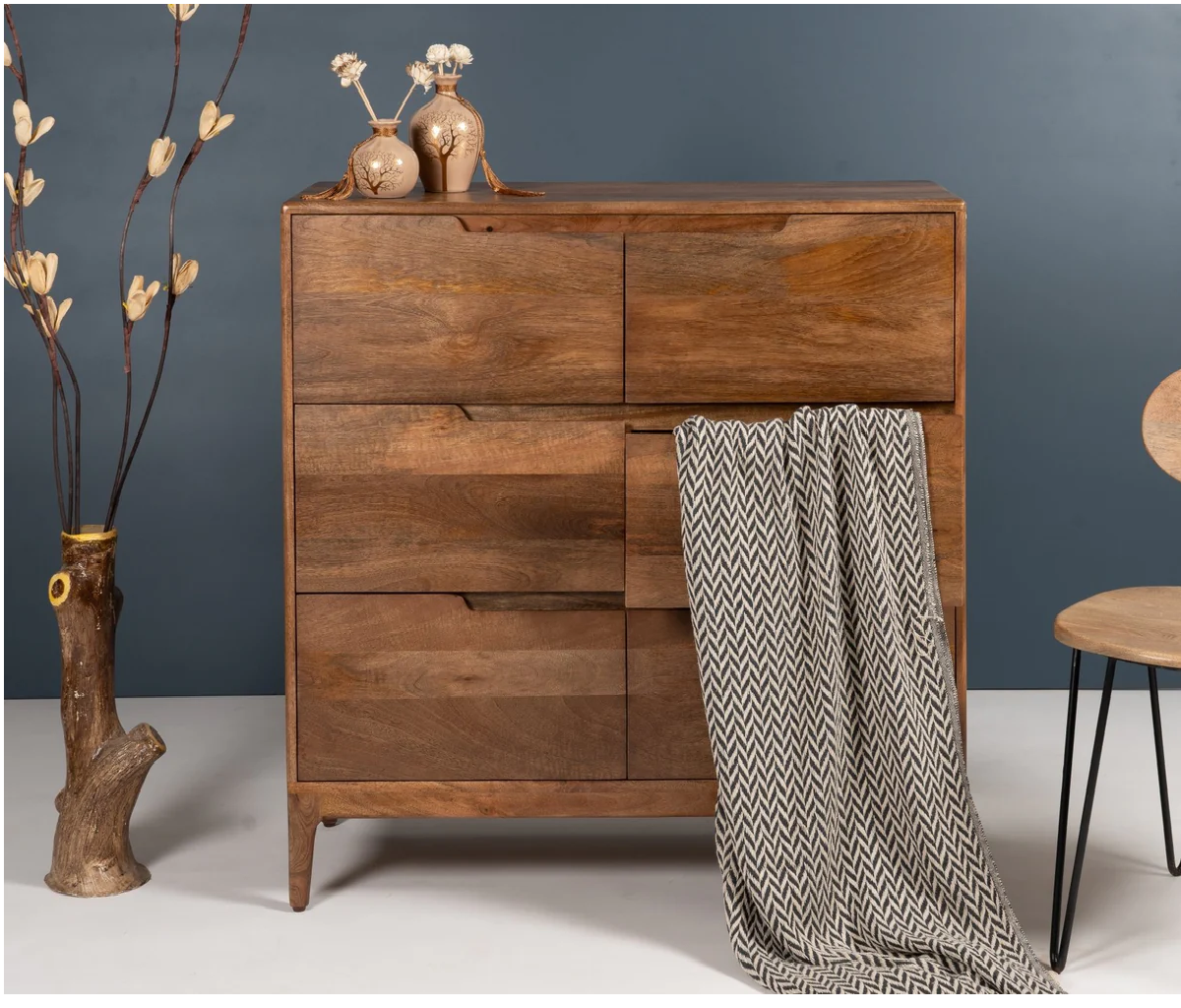 Wooden dresser with a patterned blanket draped over it against a dark blue wall.