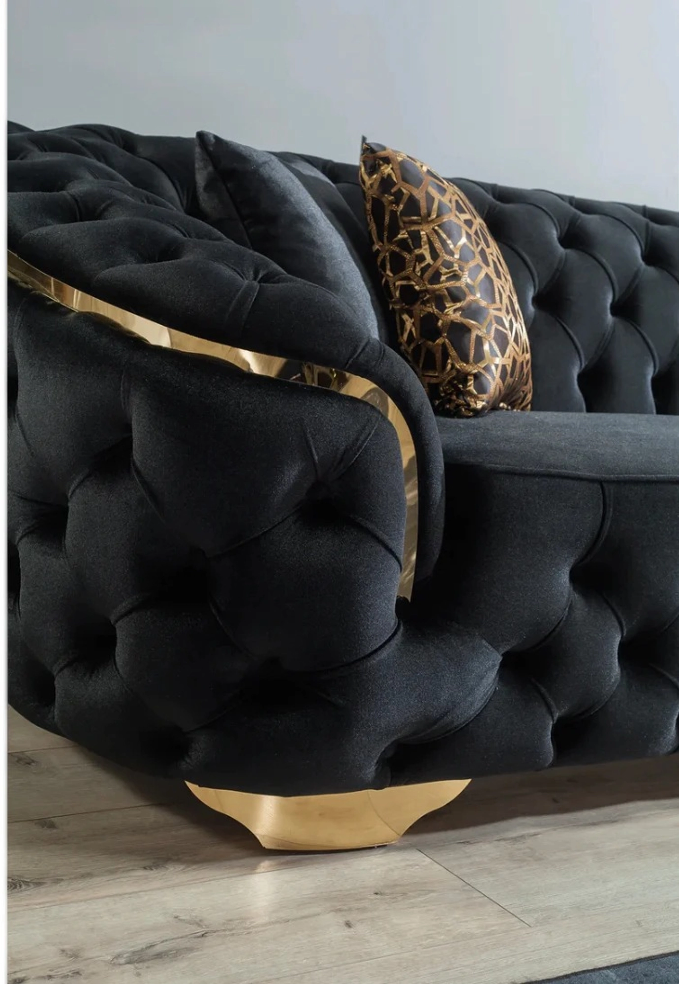 Black tufted sofa with gold accents and a leopard print pillow on a light wooden floor.