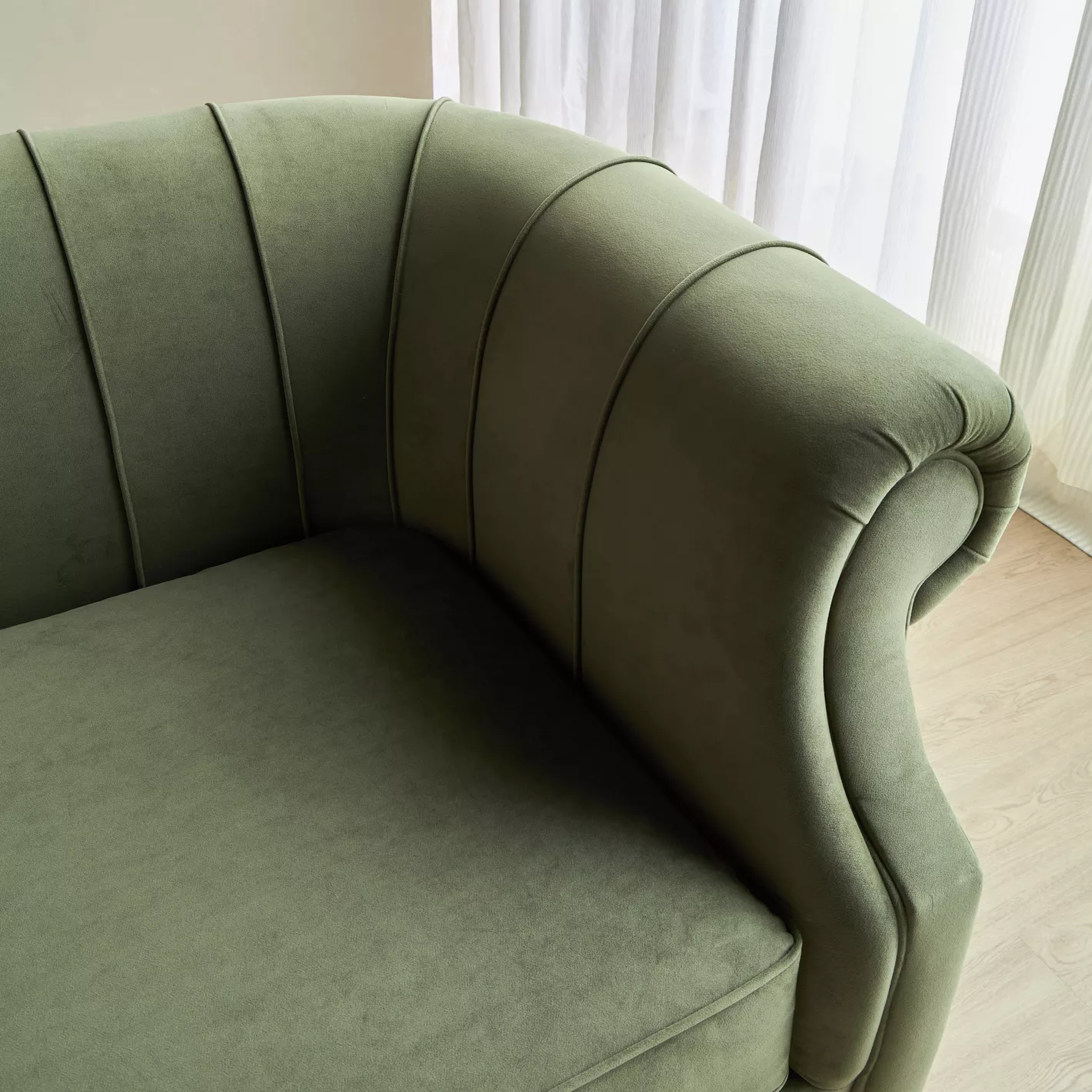 Green curved sofa in a room with light-colored curtains.