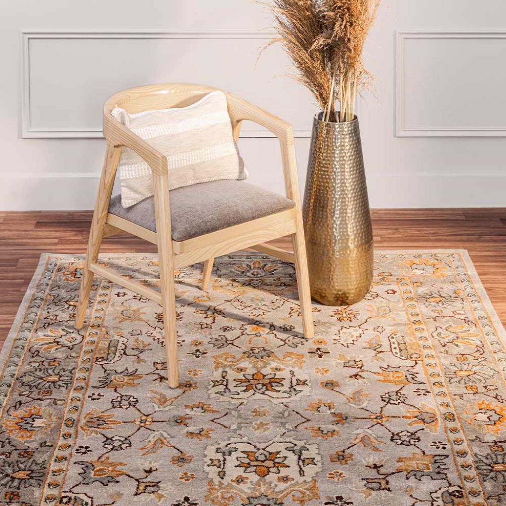 Wooden chair with a gray cushion on a patterned rug in a room with a vase and decorative elements.