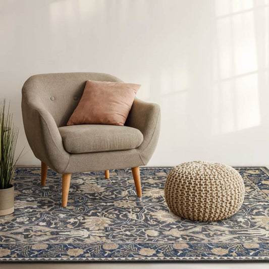 Gray armchair with a pink pillow on a patterned rug in a room with a white wall.