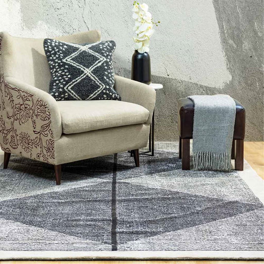 Beige armchair with decorative pillow and gray rug in a room with textured walls.