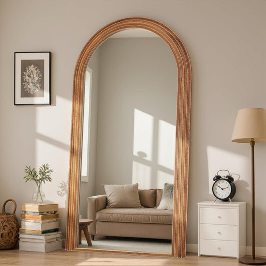 Large arched mirror with wooden frame in a room with a sofa, books, and lamp.