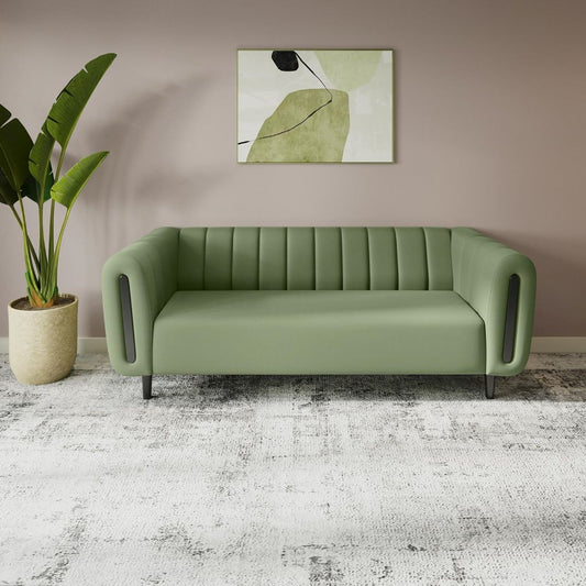 Green sofa in a room with a plant and abstract art on the wall.