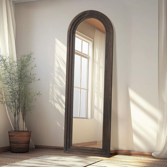 Wooden arch mirror in a room with natural light and a plant.