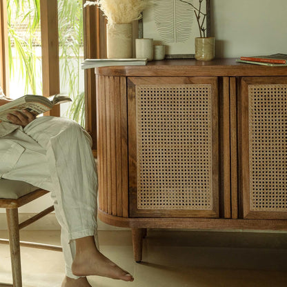 Person sitting on a chair with feet up on a wooden sideboard in a bright room.