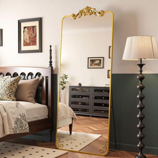 Gold-framed mirror in a bedroom with bed, lamp, and dresser.