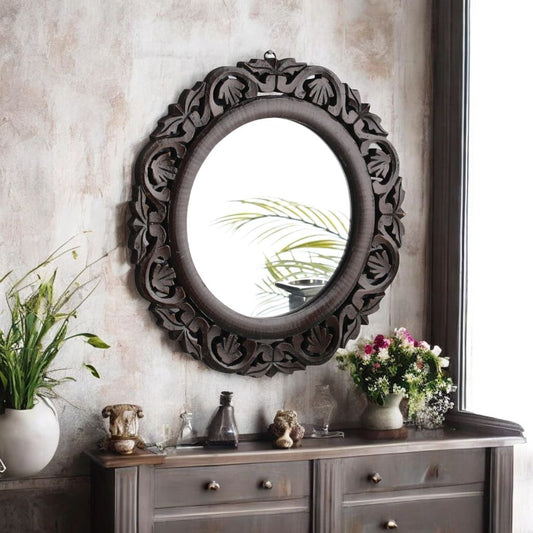 Decorative wall mirror with intricate carvings on a wall above a wooden cabinet.