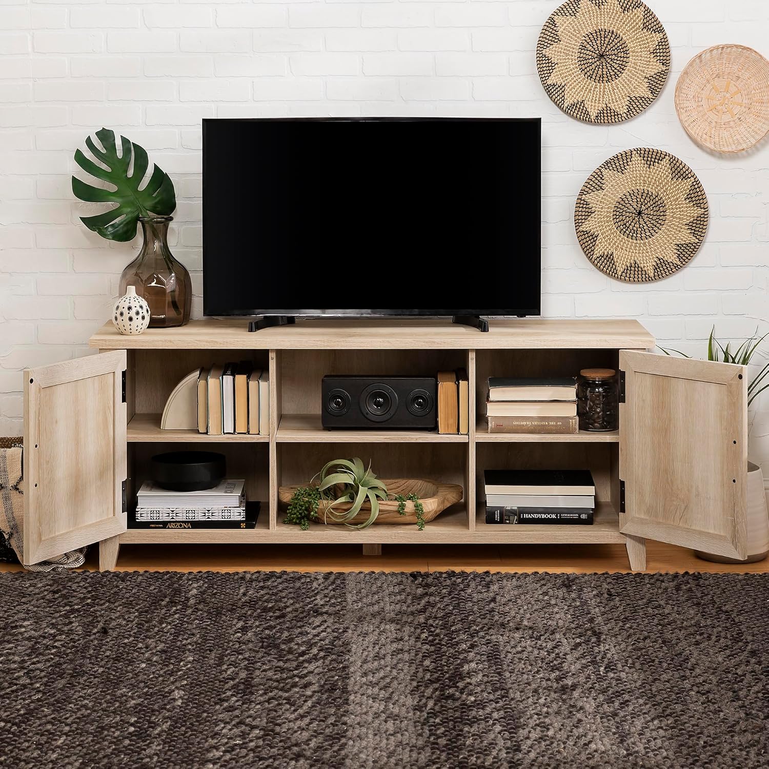 Wooden entertainment console with a TV and decorative items against a white brick wall.