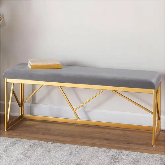 Gray cushioned bench with gold metal frame on a wooden floor against a white wall.