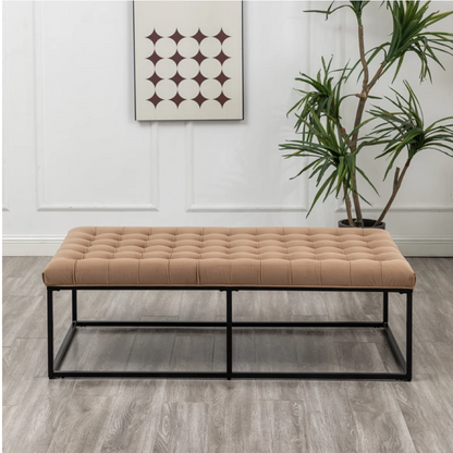 Beige tufted bench with black metal frame in a room with a plant and wall art.