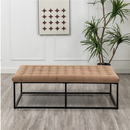 Beige tufted bench with black metal frame in a room with a plant and wall art.
