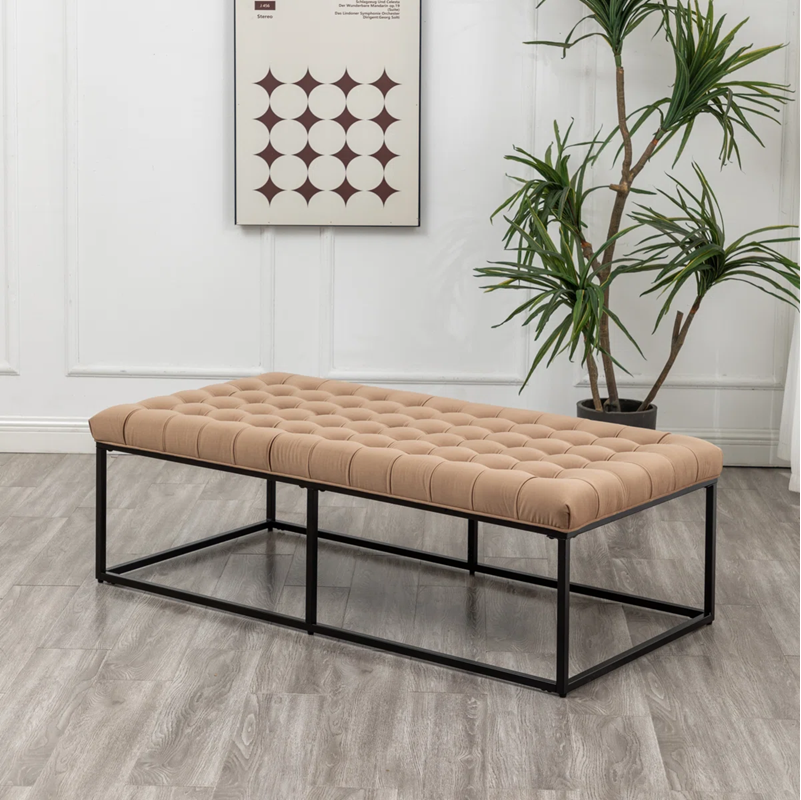 Beige tufted coffee table with black metal frame in a room with a plant and wall art.
