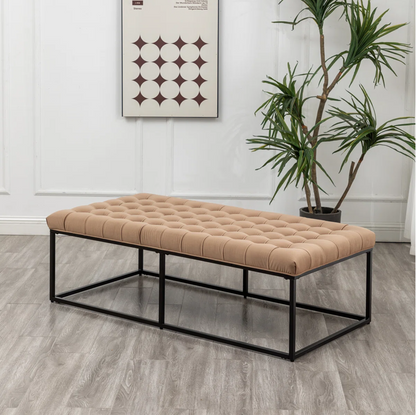 Beige tufted coffee table with black metal frame in a room with a plant and wall art.