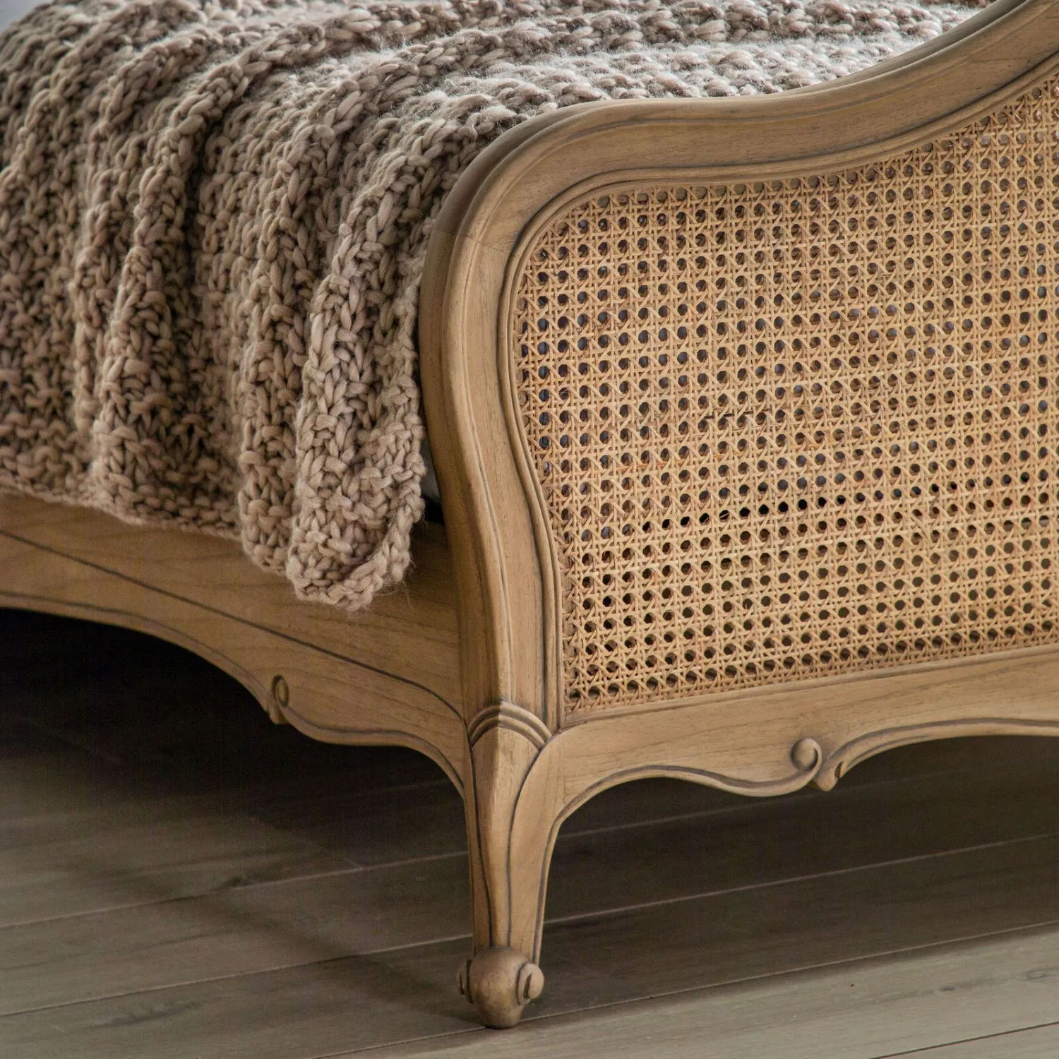 Wooden bed with wicker headboard and knitted blanket on a wooden floor