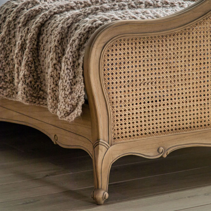 Wooden bed with wicker headboard and knitted blanket on a wooden floor