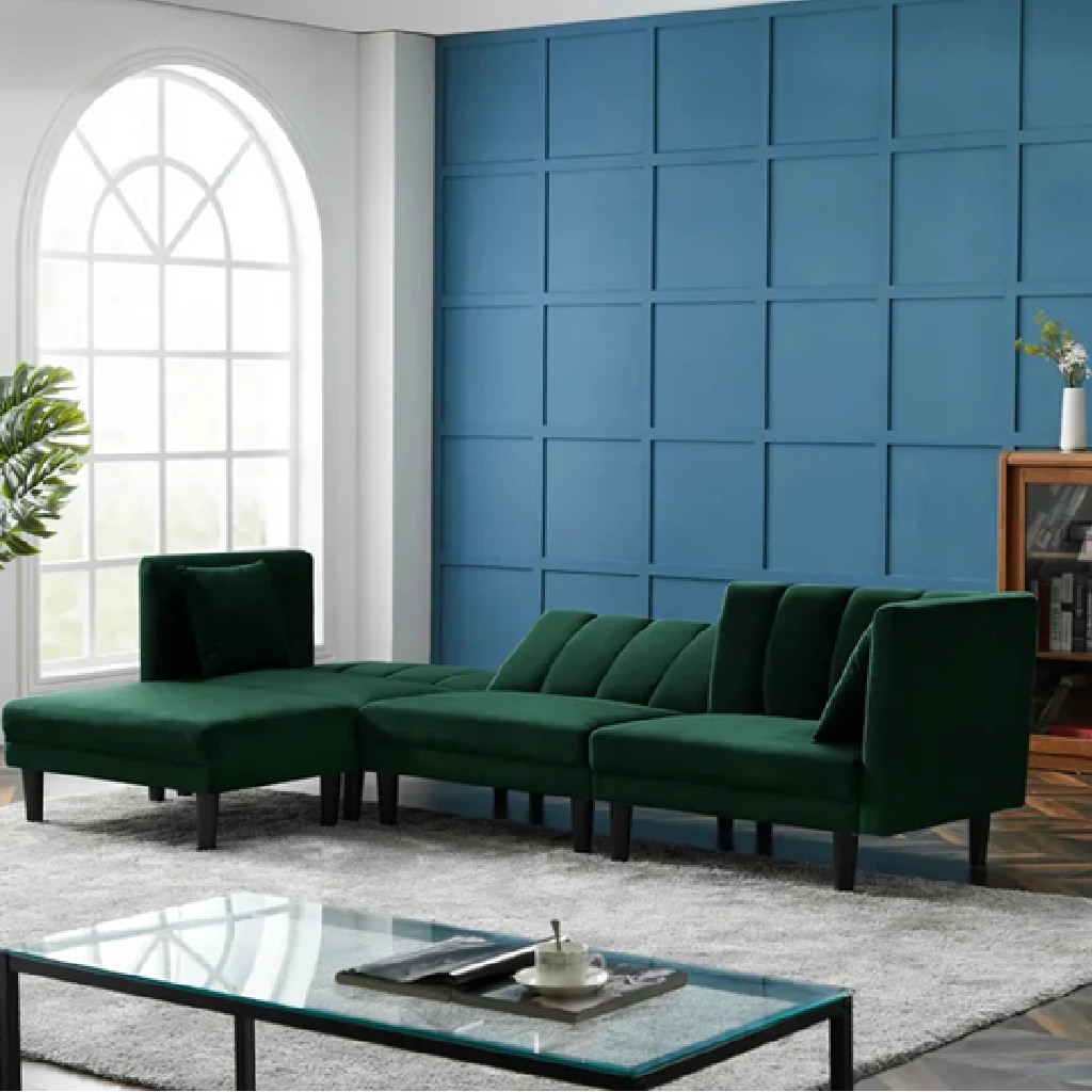 Green sectional sofa in a living room with a blue paneled wall and glass coffee table.
