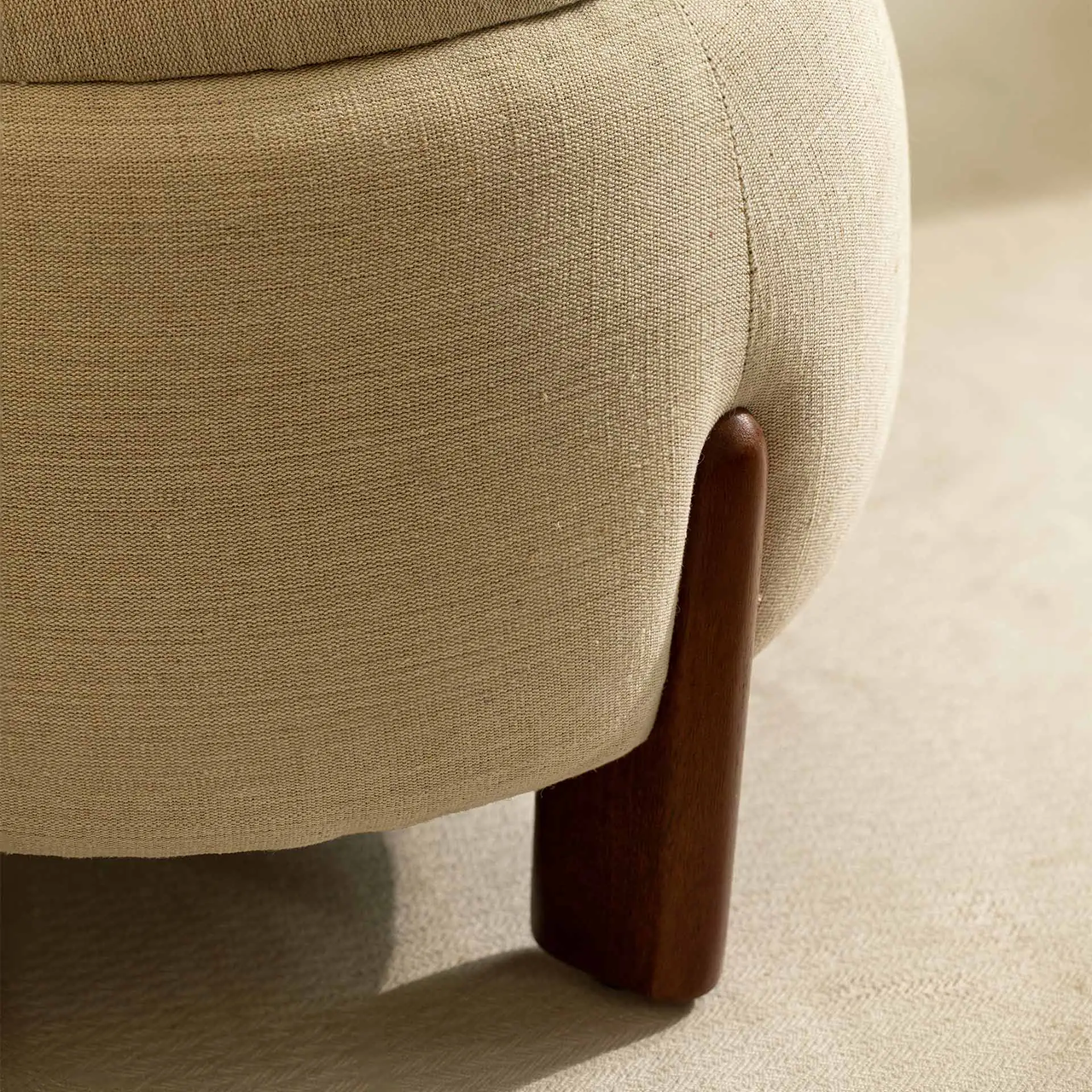 Close-up of a beige upholstered chair with a wooden leg on a neutral background