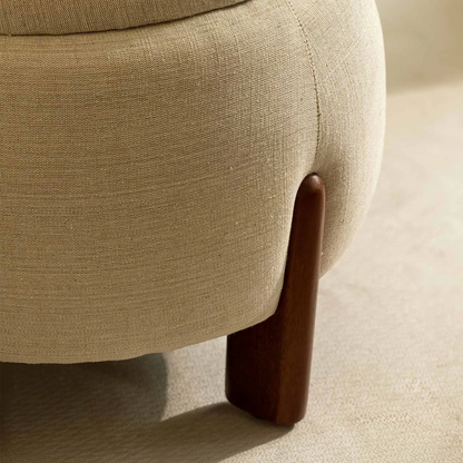 Close-up of a beige upholstered chair with a wooden leg on a neutral background