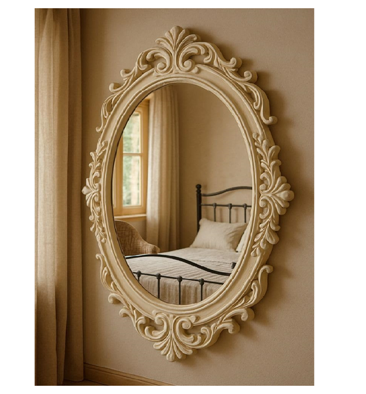 Decorative oval mirror with intricate carvings on a beige wall.