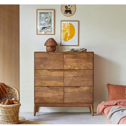 Wooden dresser in a room with framed pictures and a wicker chair.