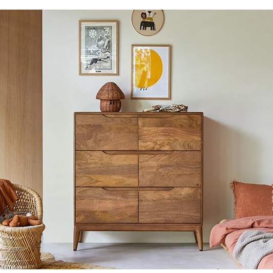 Wooden dresser in a room with framed pictures and a wicker chair.