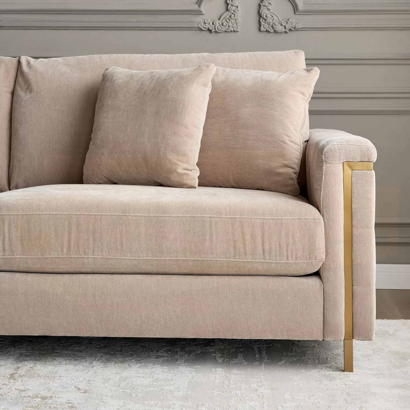 Beige sofa with gold legs in a room with decorative wall molding.