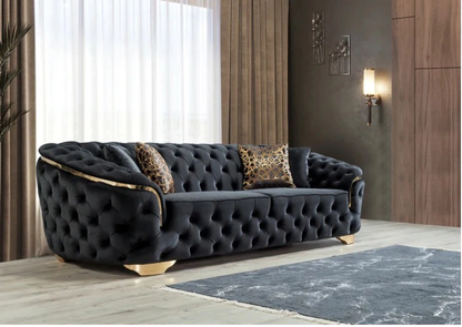 Black tufted sofa with leopard print pillows in a room with wooden floor and wall.