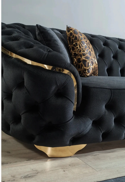 Black tufted sofa with gold accents and a leopard print pillow on a light wooden floor.